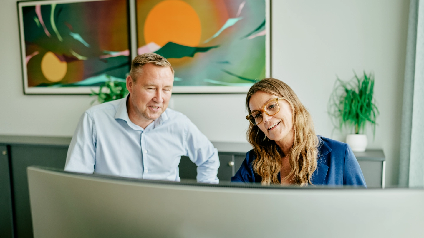 Woman and man discussing behind a desk with curved screen dk