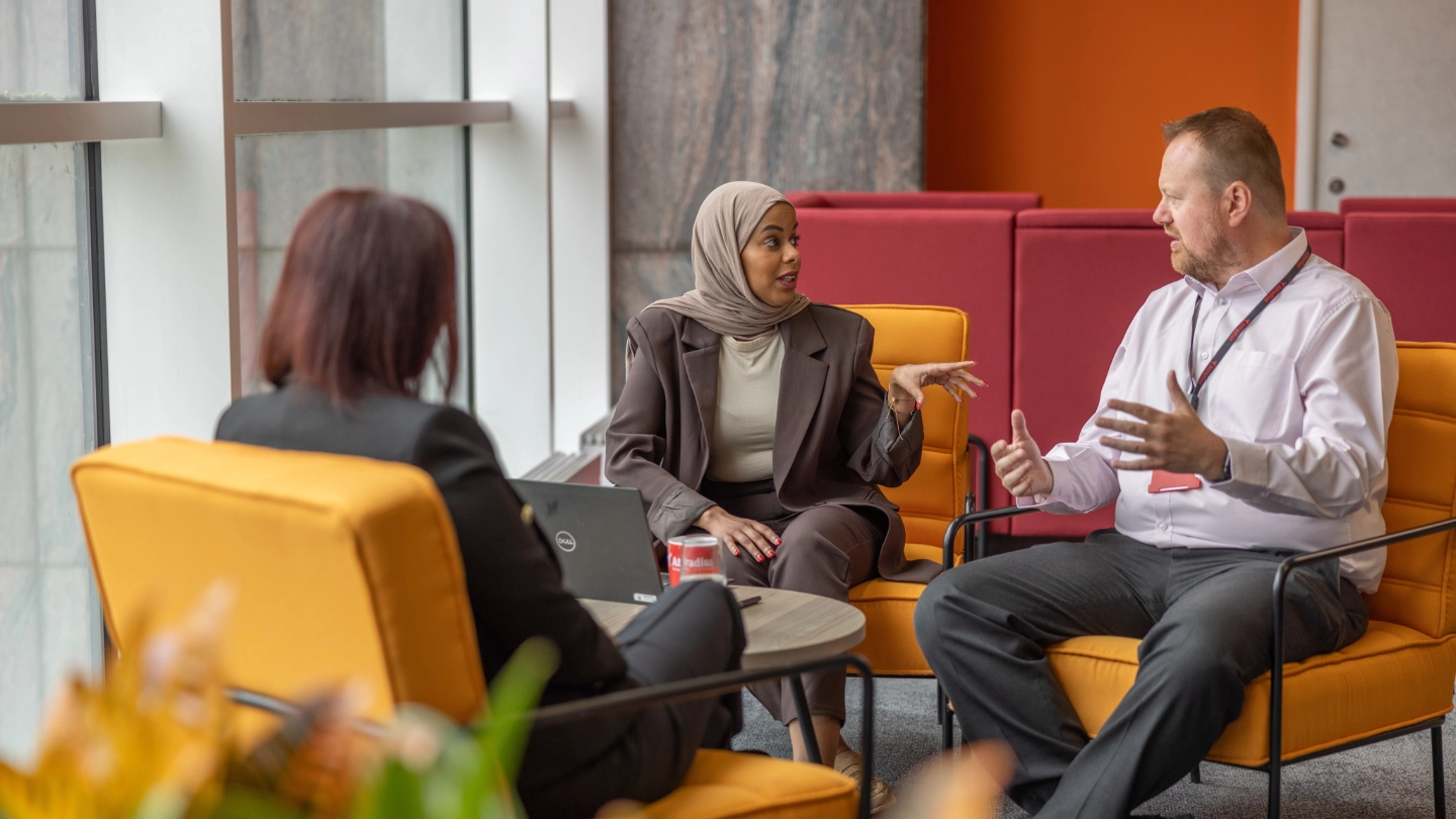 Two women and man on orange seats meeting